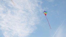 4K multicoloured kite flying in blue sky under gusts of wind with some white clouds up high. Hobbies and leisure activities concept.