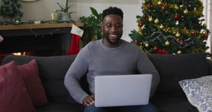 Smiling african american man having video call, sending kisses, christmas decorations in background. christmas, festivity and tradition at home.