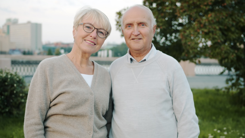 Portrait of elderly married couple smiling standing outside in urban street and looking at camera with happy faces. City lifestyle and relationship concept.
