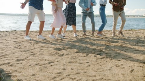 Slow motion of creative millennials jumping and dancing on beach having fun together relaxing on summer day. Cheerful youth and leisure activities concept.