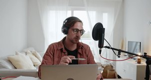 Caucasian male recording podcast in living room using laptop and microphone