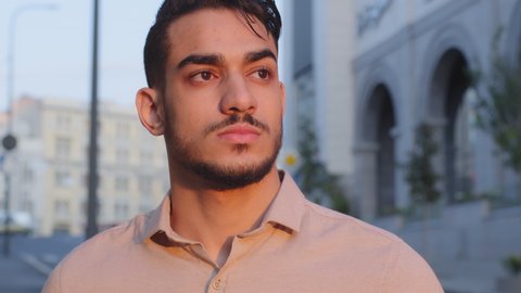 Extreme close-up male serious sad face attractive young successful pensive bearded arab business man guy hispanic boss leader standing in city on street outdoors looking in distance thinking dreaming