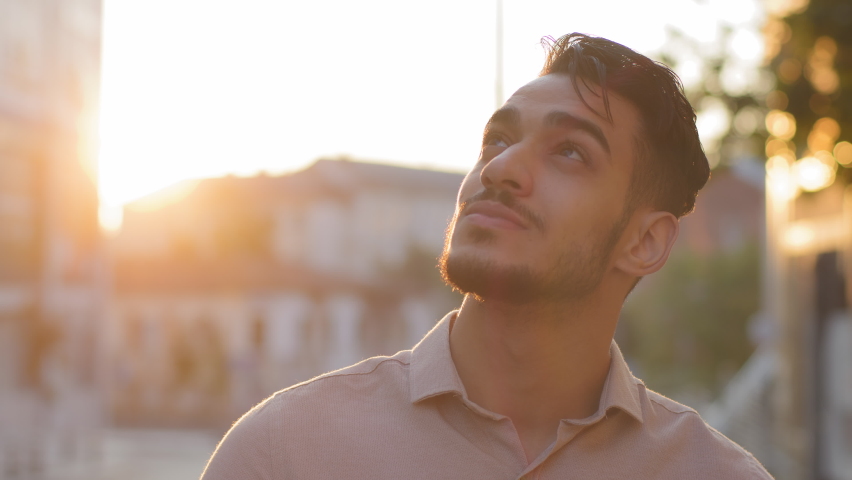 Close-up ethnic indian male happy inspired bearded face. Portrait arabic hispanic business man young adult pensive guy stands in city on street background of sunset sun dreaming thinking enjoying rays | Shutterstock HD Video #1079636534