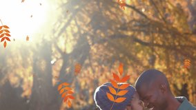 Animation of orange autumn leaves falling over happy african american couple in park. seasons, autumn, fall, colour and nature concept digitally generated video.