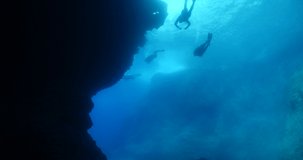 scuba divers around a reef underwater deep blue water big rocks and bubbles ocean scenery