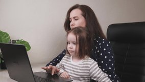 a business woman freelancer works at a laptop with a small daughter, kid prevents the mother from studying online using a computer, ordering from an online store, child is capricious with her mom