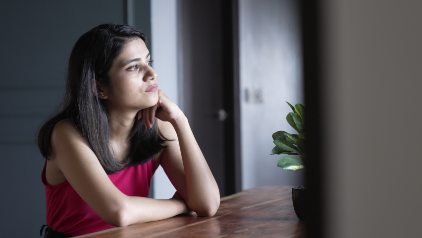 Portrait of Beautiful Young Indian Woman looking away thinking of a problem keeping a hand on her face feeling lonely at home. Upset indian girl feeling confused and depressed.