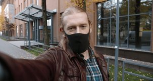 Cheerful caucasian man in medical mask standing on street in quarantine and talking on video call. Close up portrait of handsome guy video chatting outdoor. Conversation concept
