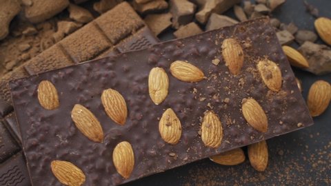 Cooking chocolate bars with almonds, desserts, handmade sweets. Composition of bars and pieces milk and dark chocolate, grated cocoa on black background top view. Confectionery craft on table