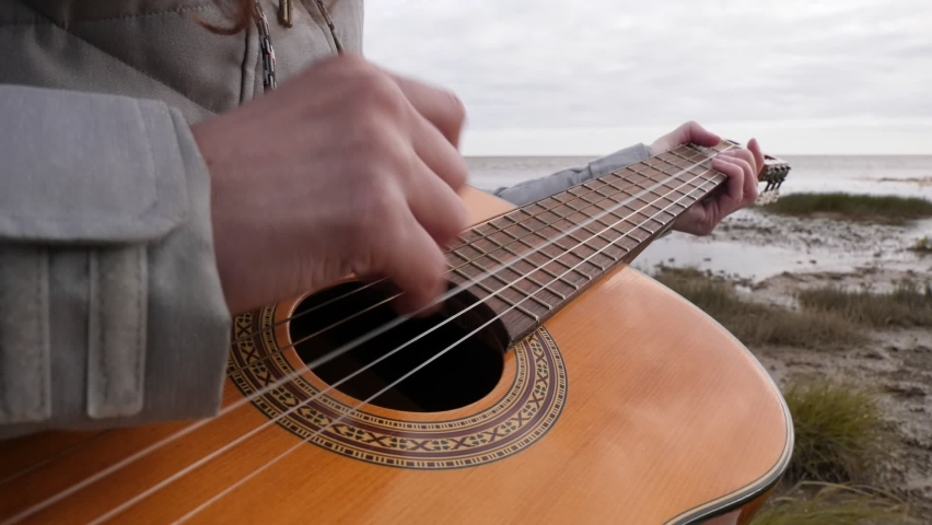 Woman Plays Guitar on the Lake Shore. Windy Weather on the Shore. Playing Musical Instruments.