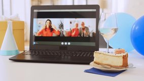 people, technology and online communication concept - laptop with family having video call or virtual birthday party on screen, cake, gift box and coffee on table at home