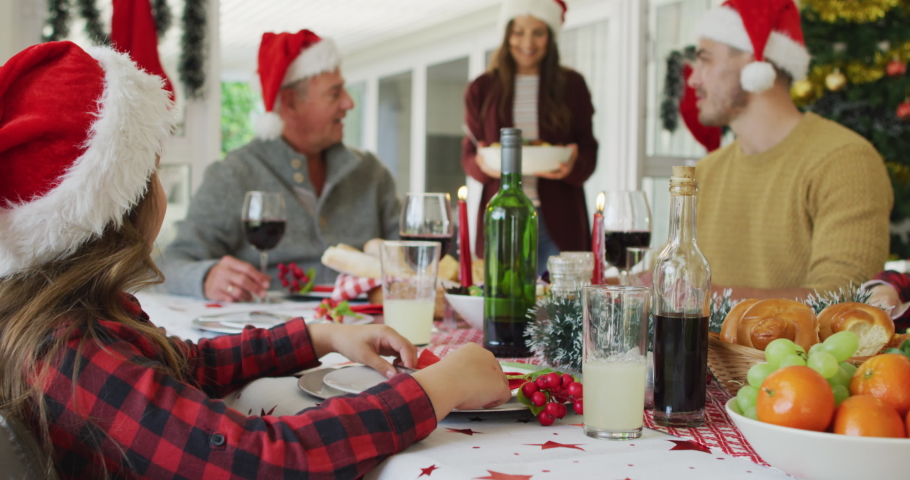 Happy caucasian multi generation family wearing santa hats, having christmas meal. family christmas time and festivity together at home.