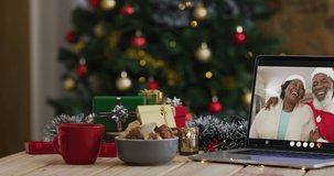 African american senior couple wearing santa hats on video call on laptop, with christmas tree. christmas, festivity and communication technology digital composite video.