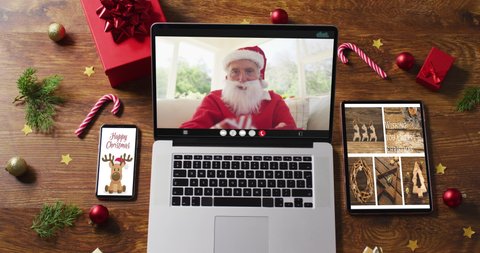 Happy senior caucasian santa on video call on laptop, with smartphone, tablet christmas decorations. christmas, festivity and communication technology digital composite video.