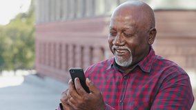 Happy contented senior black grandfather man making video call, looking at smartphone camera, showing thumb up approval gesture, african american mature tell good news talking on modern mobile phone