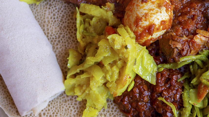 Pan across Injera served with chicken, egg, doro wat, berbere, vegetables and lentils. Injera, a traditional staple food of Ethiopia, is a sourdough flatbread made from teff flour. Royalty-Free Stock Footage #1079675243