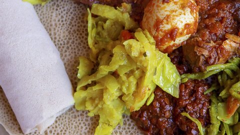 Pan across Injera served with chicken, egg, doro wat, berbere, vegetables and lentils. Injera, a traditional staple food of Ethiopia, is a sourdough flatbread made from teff flour.