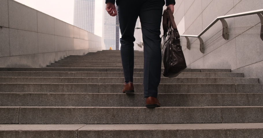 back view Businessmen put on a black suit at the office. The man holding business handbag with office formal suit walking outdoor in urban city. Legs of a business man wearing brown shoes walking up Royalty-Free Stock Footage #1079682401