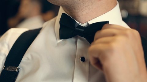 Confident successful Caucasian man in an expensive elegant formal suit adjusts his bow tie with his hand. Preparation for the official event. Men's style. Gentleman