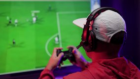 Rear view young Player video computer pc. Young man sitting on chair in game station holding joystick. Streamer man wearing headphone playing football game online in the darkroom.