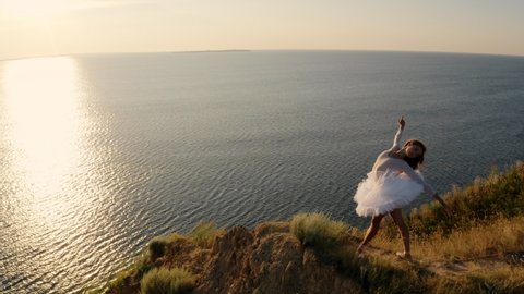 Young ballerina standing on a Cape. Women in Ballet tutu dancing at Sunrise. Aerial view of beautiful seaside Landscape. Flying above clay cliff