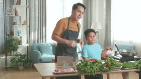 Asian Father And Son Streaming Live Video With Camera To Share Online While Cooking At Home, Boy Putting Salt
