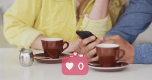 Animation of heart icons floating over caucasian couple using smartphone and drinking coffee. social media and communication interface concept digitally generated video.