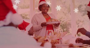 Animation of snow falling over smiling family with santa hats having dinner. christmas, winter, tradition and celebration concept digitally generated video.