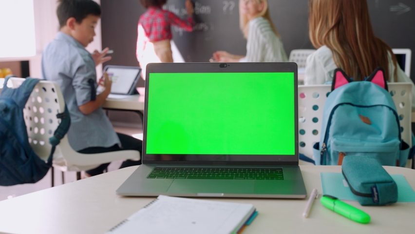 Laptop computer green blank empty mockup screen on school desk with elementary junior children students in classroom background. Education software website technology ads concept. Royalty-Free Stock Footage #1079702537