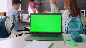 Laptop computer green blank empty mockup screen on school desk with elementary junior children students in classroom background. Education software website technology ads concept. - Powered by Shutterstock - Get 15% off with code: PIKWIZARD15