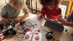 Table top view of multiethnic schoolkids building robots developing program for software robotics engineering using devices at classroom lab. AI technologies development. STEM education concept. - Powered by Shutterstock - Get 15% off with code: PIKWIZARD15