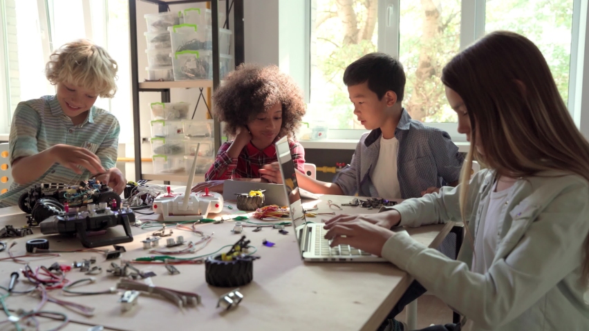 Group of multieracial schoolchildren interacting using gadgets laptops for programming at robotics engineering class. School science classroom of futuristic technologies. STEM education concept. Royalty-Free Stock Footage #1079702552