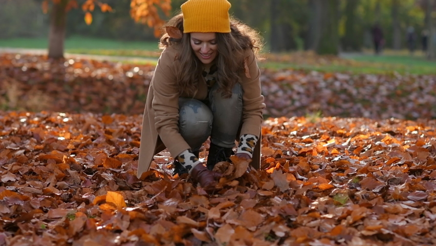 Hello autumn. smiling modern female in brown coat and yellow hat rejoicing outdoors in the city park in autumn. Royalty-Free Stock Footage #1079704427