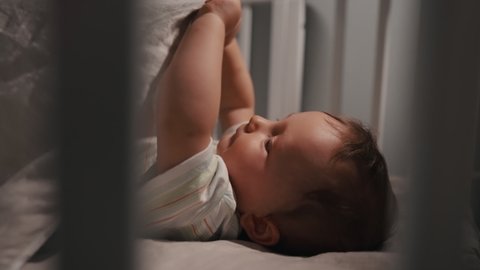 Adorable newborn baby boy, don't want to sleep in crib at night. Mother puts baby to bed.