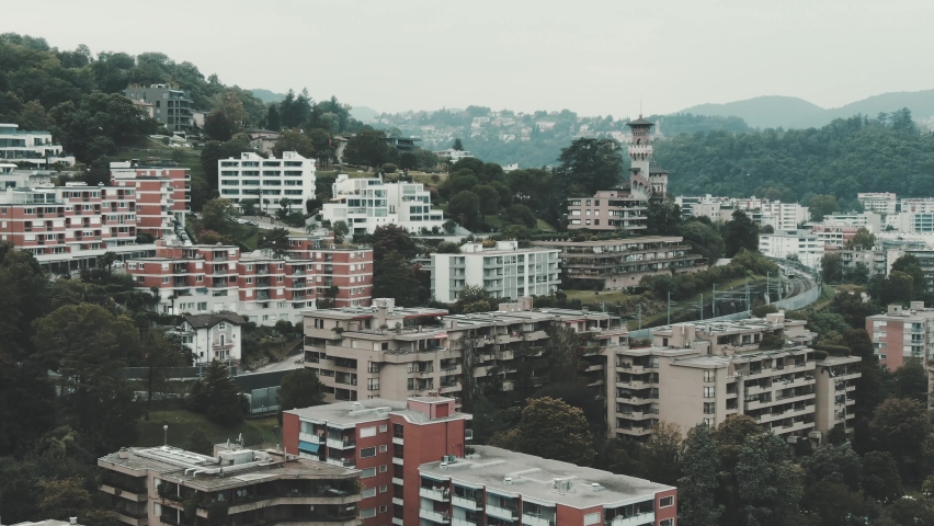 Lugano, Switzerland. Cinematic flight over the Paradiso district, with views of various buildings and an old castle tower whilst flying through a flock of seagulls.