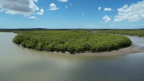 Drone aerial footage up a country creek with muddy water and banks fills with bush below a cloudy blue sky