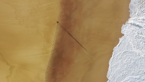 Aerial view of a tourist walking along sandy beach. Foamy waves crashing against yellowish coastline as seen from above. High quality 4k footage