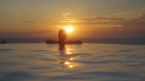 
Man silhouette swims to the pool edge enjoying sunset sea view on holidays