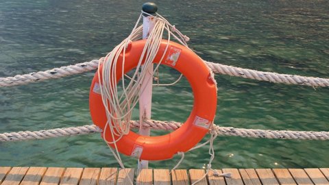 Orange lifeline and sea ropes on the background of the sea and blue sky. Marine ropes and life preserver hanging on a post. Help and safety concept