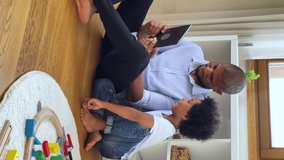African family mixed-race boy his dad spend time on internet, sit on warm floor in cozy playroom with digital tablet, having fun online, play video games, enjoy leisure use modern tech, vertical view