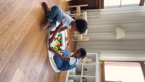 Vertical view two siblings African boy girl sit on floor play together wooden railroad, build rail road connects parts of playthings prepare toy set for playtime at home. Development, leisure concept