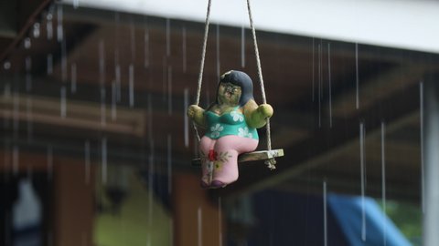 Chanthaburi, Thailand,September 24, 2021: Colse-up A doll sits on a swing while it rains, which looks sad.