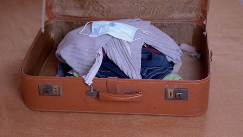 Large Pile of Things Thrown in an Open Old Suitcase Along with a Mask. Things are stacked randomly in a brown travel suitcase that closes quickly. Travel concept with coronavirus protection means. 4K.