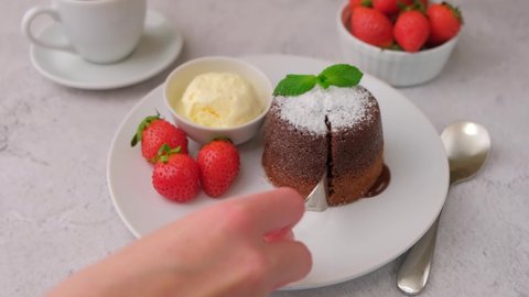 Lava cake with dripping filling. Chocolate fondant cake with vanilla ice cream, strawberries, mint, and coffee. Traditional French pastries. The woman cuts the cake and the filling flows out of it. Close-up