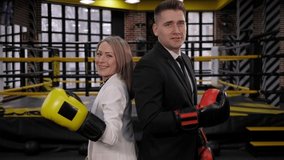 Portrait of a happy businessman and a woman in business suits with boxing gloves, they are standing against the background of a boxing ring and dancing. Success in business. - Powered by Shutterstock - Get 15% off with code: PIKWIZARD15