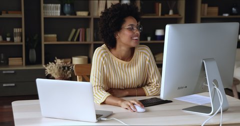 Mixed race female remote employee use two computers at online office work synchronize data within integrated domestic network. Young black businesswoman share files between laptop desktop pc devices