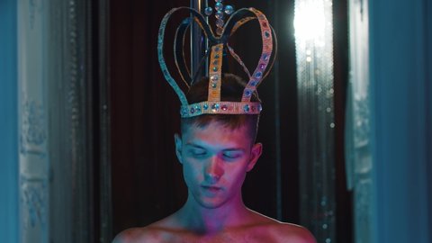 Shirtless man wearing a crown on his head and eating candy - neon lighting
