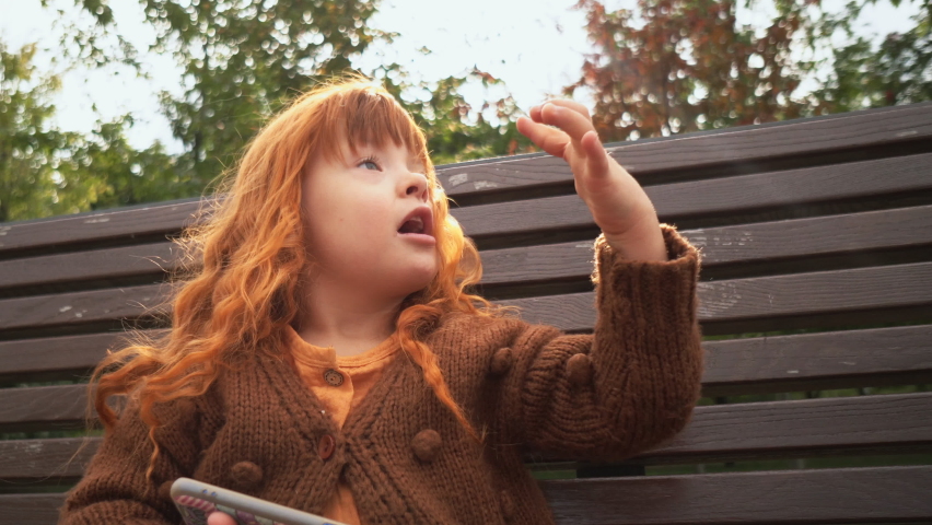 Toddler girl with down syndrome sitting on the bench and playing on smartphone | Shutterstock HD Video #1079736830