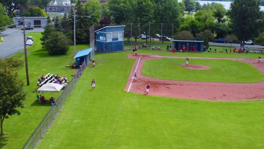 Baseball game in a town ball park Red team in bases Camera in right field Looking towards 1st base Left till  Summer day Drone
