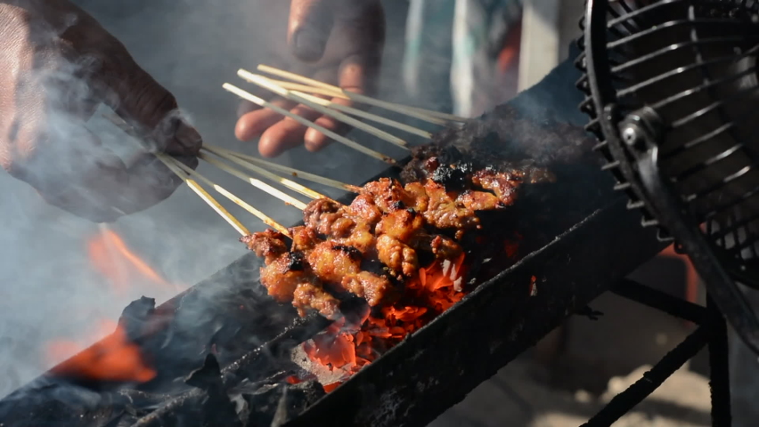 Chicken satay on traditional charcoal fire. satay on fire with smoke and an appetizing look. hands cooking satay on the grill Royalty-Free Stock Footage #1079738156